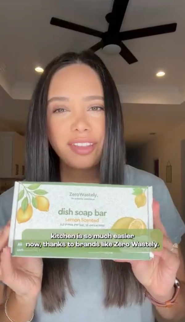 Woman holding a box of zerowastely dish soap bars with text overlay in a kitchen setting